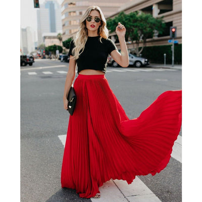 Femme élégante en jupe longue rouge plissée, haut noir, lunettes de soleil, marchant en ville. Mode urbaine chic, style tendance.