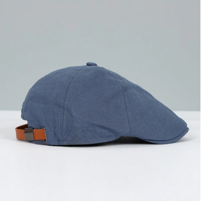 Casquette plate bleue en coton avec sangle réglable en cuir marron, style rétro élégant, accessoire de mode pour homme, fond gris clair.