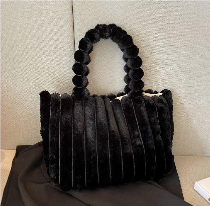 Sac à main en fourrure noire avec anses perlées, posé sur un canapé beige. Accessoire élégant et tendance, idéal pour l'hiver.