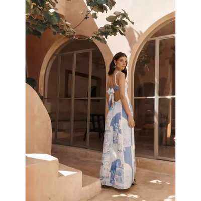 Robe longue dos nu bleue et blanche à motifs, portée par une femme devant une maison méditerranéenne avec arches et plantes grimpantes.