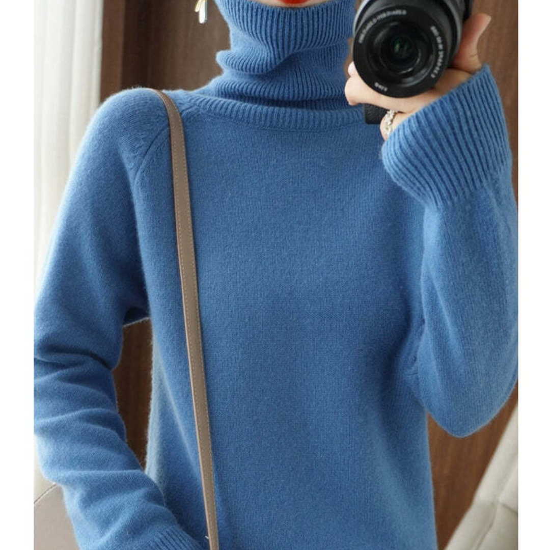 Pull bleu en laine à col roulé, manches longues, porté par une personne tenant un appareil photo. Mode hiver, style décontracté et élégant.