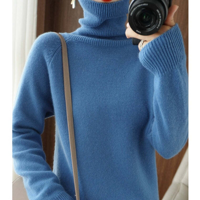 Pull bleu en laine à col roulé, manches longues, porté par une personne tenant un appareil photo. Mode hiver, style décontracté et élégant.