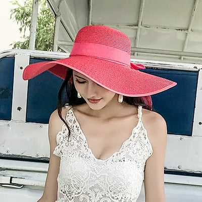Femme portant un chapeau de soleil rose vif, robe en dentelle blanche, assise dans un véhicule. Mode estivale, élégance, accessoires tendance.