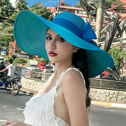 Jeune femme portant un grand chapeau bleu, robe blanche, en ville. Mode estivale, élégance, style urbain, chapeau large, tendance féminine.