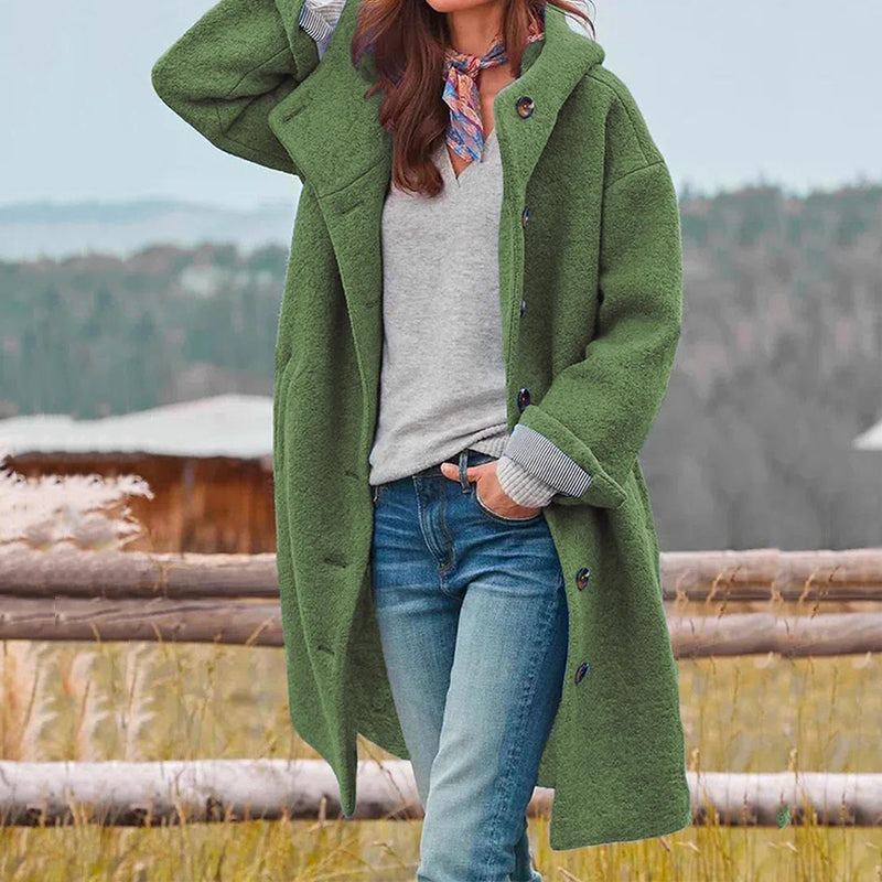 Femme portant un manteau vert en laine, chemise grise et jean, posant devant un paysage rural. Mode automne, style décontracté, tendance 2023.