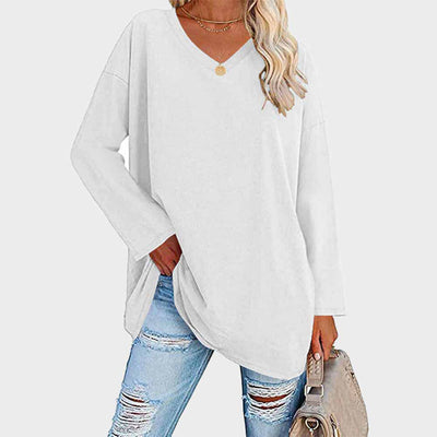 Femme portant un pull blanc ample à col en V, associé à un jean déchiré bleu clair et un sac beige. Mode décontractée, tendance automne.