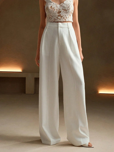 Femme en pantalon blanc ample et top en dentelle, posant dans un intérieur minimaliste. Mode élégante, tenue chic, style contemporain.
