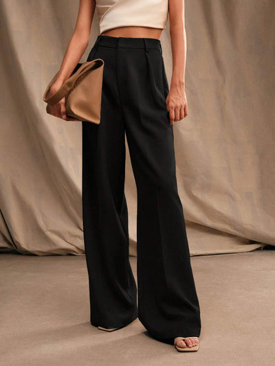 Femme portant un pantalon noir large et un haut blanc, tenant un sac à main beige. Mode élégante, style minimaliste, tenue chic.