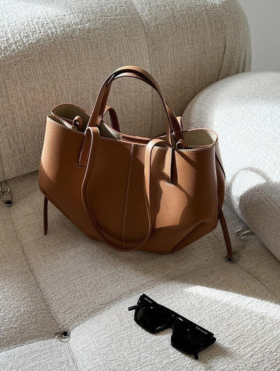 Sac à main en cuir marron sur canapé beige, avec lunettes de soleil noires à côté. Accessoire mode élégant, tendance et chic pour femme.