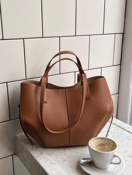Sac à main en cuir marron sur une table en marbre blanc, avec une tasse de café vide à côté. Élégant, moderne, accessoire de mode tendance.