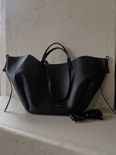 Sac à main noir en cuir élégant posé sur une surface blanche, accompagné de lunettes de soleil noires. Accessoire mode chic et moderne.