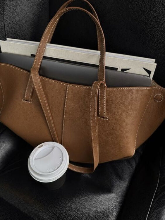 Sac à main en cuir marron sur siège noir avec ordinateur portable et gobelet café. Accessoire mode élégant, bureau mobile, style moderne.