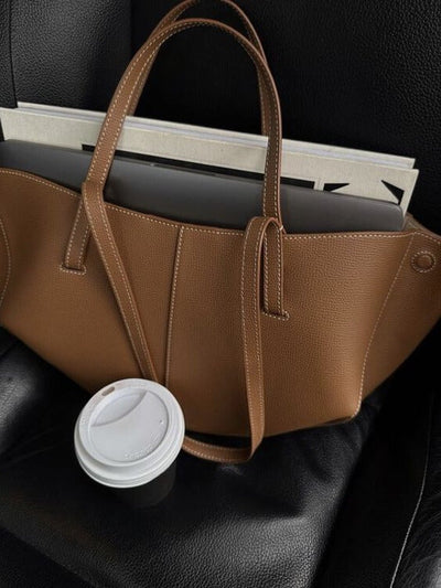 Sac à main en cuir marron sur siège noir avec ordinateur portable et gobelet café. Accessoire mode élégant, bureau mobile, style moderne.