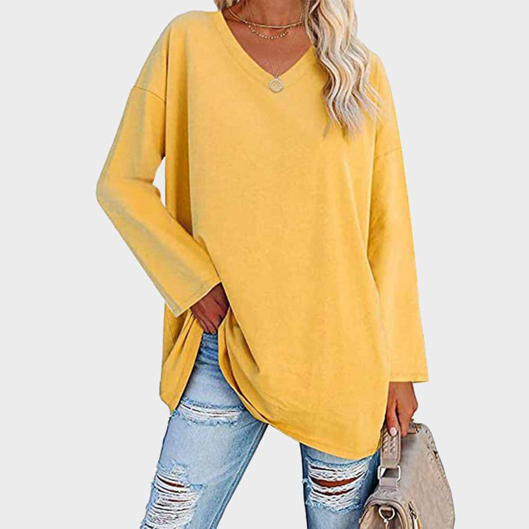 Femme portant un pull jaune ample avec un col en V, associé à un jean déchiré et un sac beige. Mode décontractée, tendance automne.
