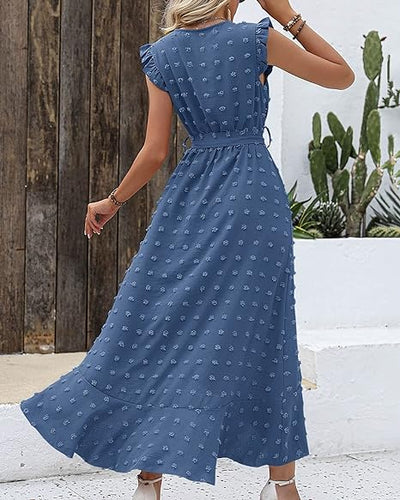 Robe longue bleue à motifs floraux, manches courtes à volants, ceinture à nouer, femme de dos, cactus en arrière-plan, style bohème chic.