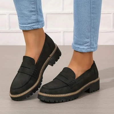 Chaussures mocassins noirs pour femme avec semelle épaisse, portées avec un jean bleu clair. Style décontracté et moderne.