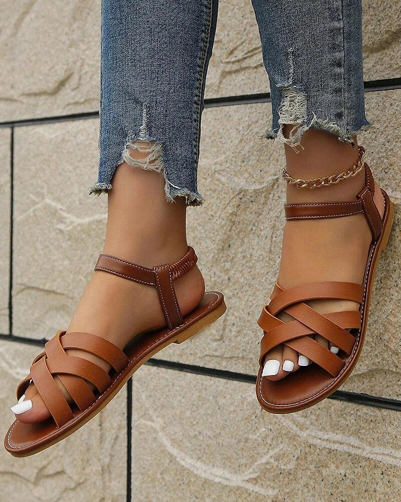 Sandales en cuir marron pour femme, style gladiateur, portées avec un jean déchiré. Chaussures d'été tendance et confortables.