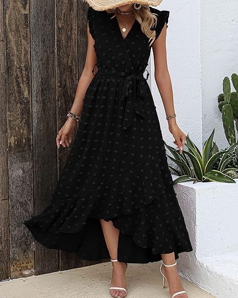 Robe longue noire à pois, sans manches, ceinturée, portée par une femme. Style élégant et décontracté, idéale pour l'été. Plantes en arrière-plan.
