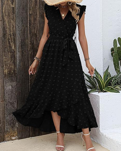 Robe longue noire à pois, sans manches, ceinturée, portée par une femme. Style élégant et décontracté, idéale pour l'été. Plantes en arrière-plan.