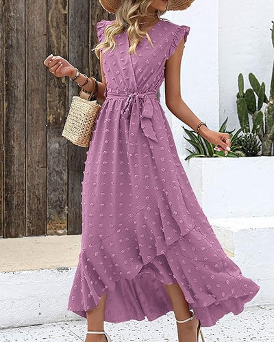 Robe longue violette à volants, motif floral, portée par une femme avec un chapeau de paille et un sac en osier, style estival élégant.