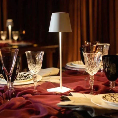Lampe de table moderne éclairant une table élégante avec verres en cristal et vaisselle raffinée, ambiance chaleureuse et sophistiquée.