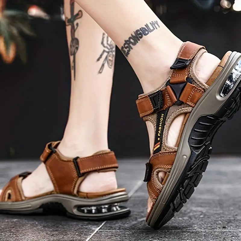 Sandales de randonnée marron pour homme avec semelle amortissante, design sportif, portées par une personne tatouée. Chaussures confortables et robustes.