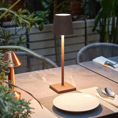 Lampe de table moderne en métal sur une terrasse élégante, entourée de plantes vertes. Décoration extérieure, éclairage design, ambiance conviviale.