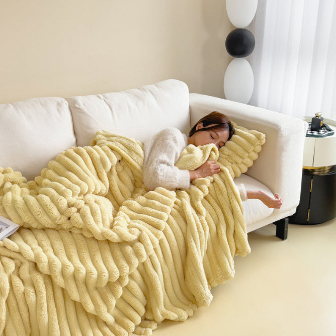Femme endormie sur un canapé blanc, enveloppée dans une couverture jaune en peluche. Décor moderne, ambiance cosy et chaleureuse.