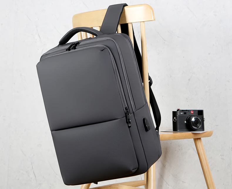 Sac à dos noir moderne sur chaise en bois, avec appareil photo vintage à côté. Design minimaliste, idéal pour voyage et photographie.