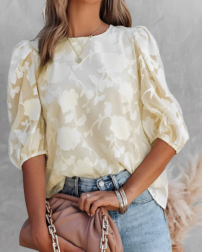 Femme portant un chemisier en dentelle blanche à manches bouffantes, tenant un sac à main beige. Mode élégante, tenue décontractée chic.