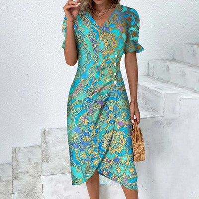 Robe d'été turquoise à motifs floraux dorés, manches courtes, portée par une femme tenant un sac en osier, debout sur des escaliers blancs.