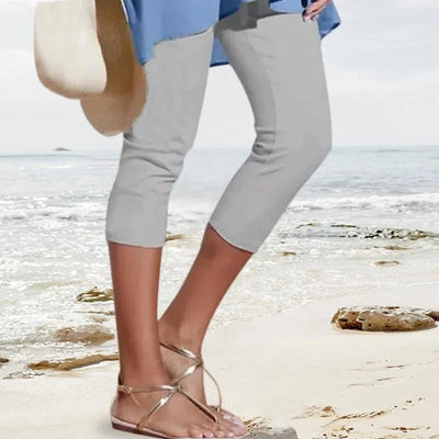Femme en pantacourt gris et sandales dorées marchant sur une plage, tenue estivale, mode plage, style décontracté, bord de mer.