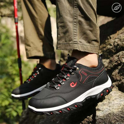 Chaussures de randonnée noires pour homme, semelle antidérapante, lacets rouges, portées en extérieur sur un sentier rocheux, pantalon kaki.