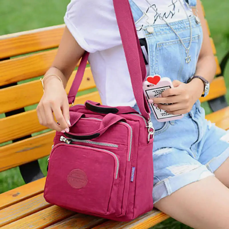 Femme assise sur un banc avec un sac à bandoulière rose vif, tenue décontractée en jean, tenant un smartphone avec un étui cœur.