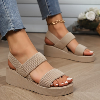 Sandales compensées beiges en tissu texturé sur pieds féminins, portées avec un jean. Chaussures d'été tendance, confortables et élégantes.