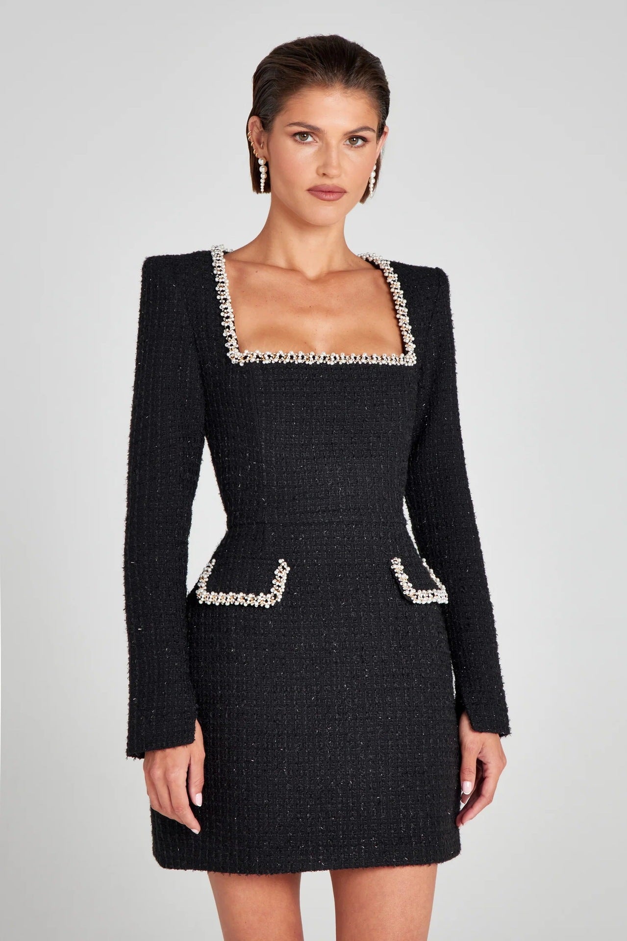 Robe noire élégante en tweed avec col carré et bordures perlées, manches longues, poches décoratives, portée par une femme. Mode chic et sophistiquée.