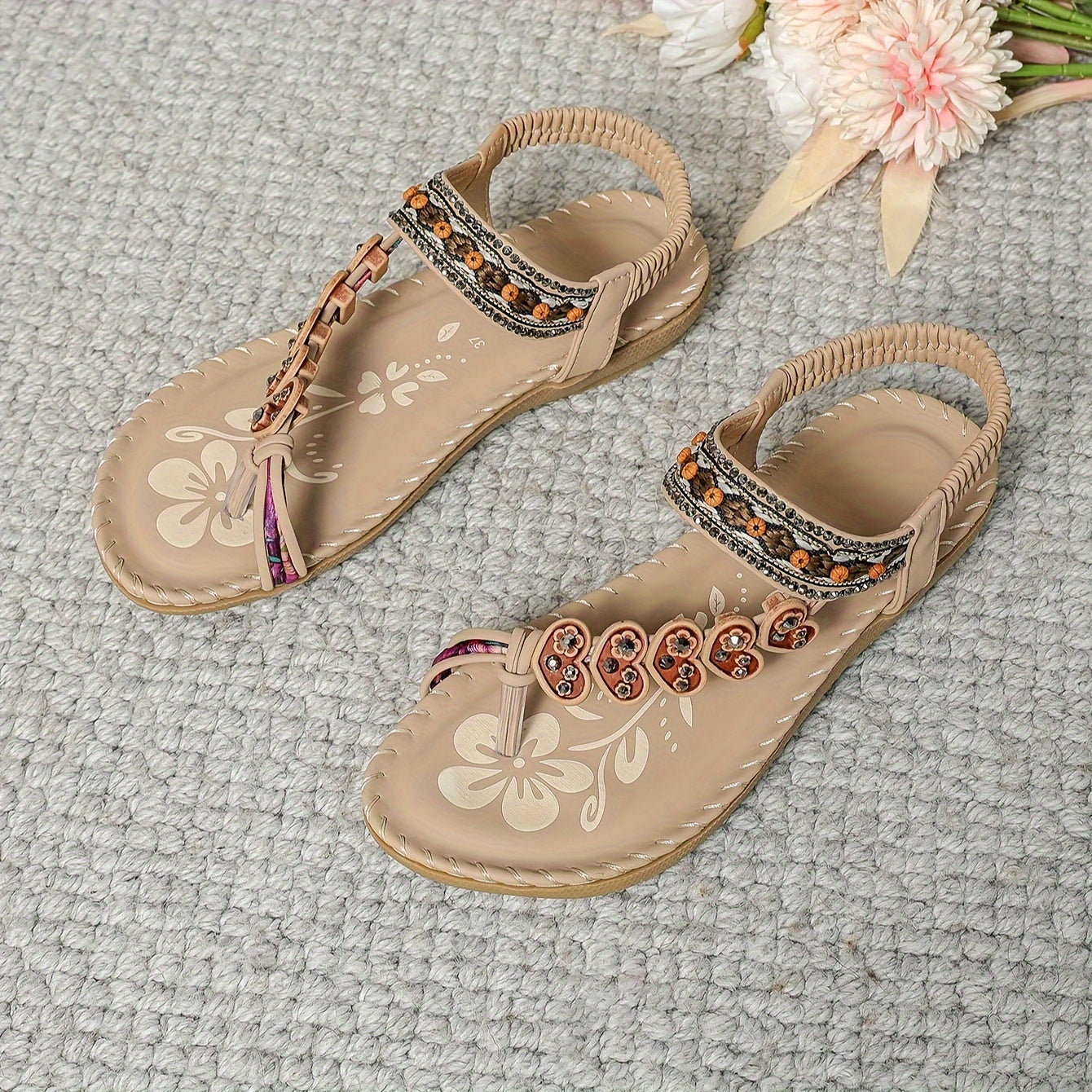 Sandales beige pour femmes avec motifs floraux et perles orange, posées sur un tapis gris. Chaussures d'été élégantes et confortables.