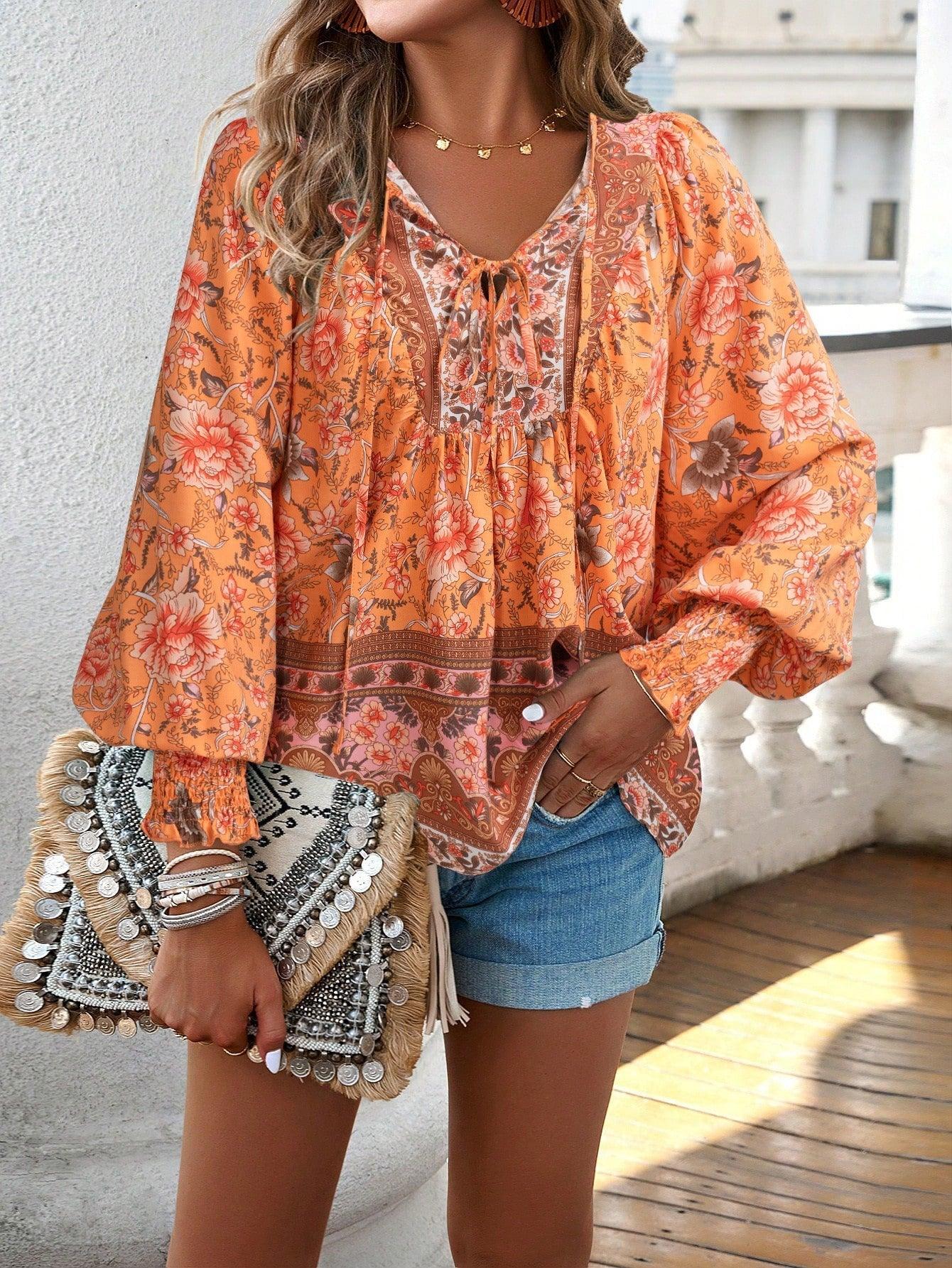 Femme portant un chemisier bohème orange à motifs floraux, short en jean, et tenant un sac à main en paille décoré de perles. Mode estivale chic.