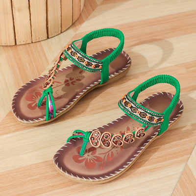 Sandales vertes élégantes avec ornements floraux et perles, posées sur un sol en bois clair. Chaussures d'été tendance pour femmes.