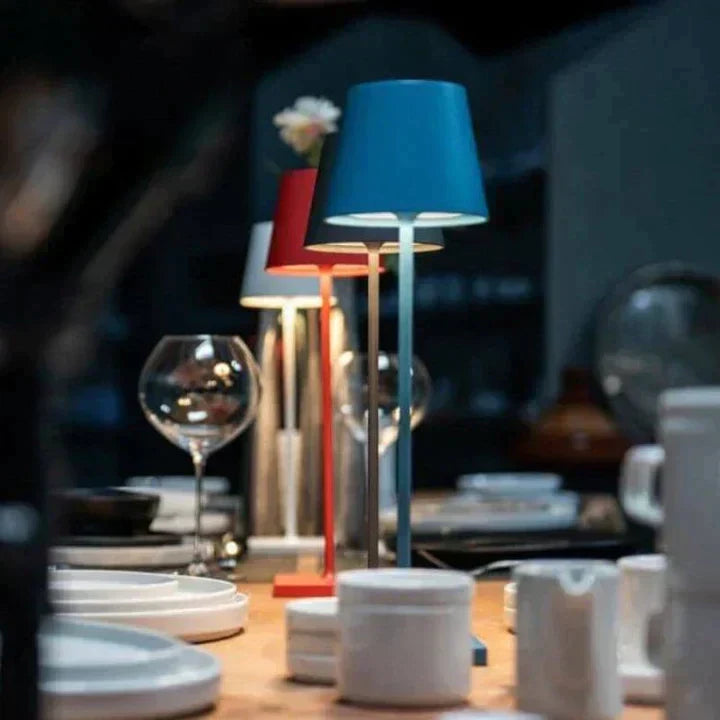 Trois lampes de table colorées éclairent une table dressée avec des verres à vin et de la vaisselle, créant une ambiance chaleureuse et moderne.