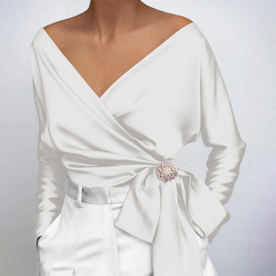 Blouse blanche élégante à manches longues, col en V, ceinture nouée avec broche florale, style chic et moderne, mode féminine tendance.