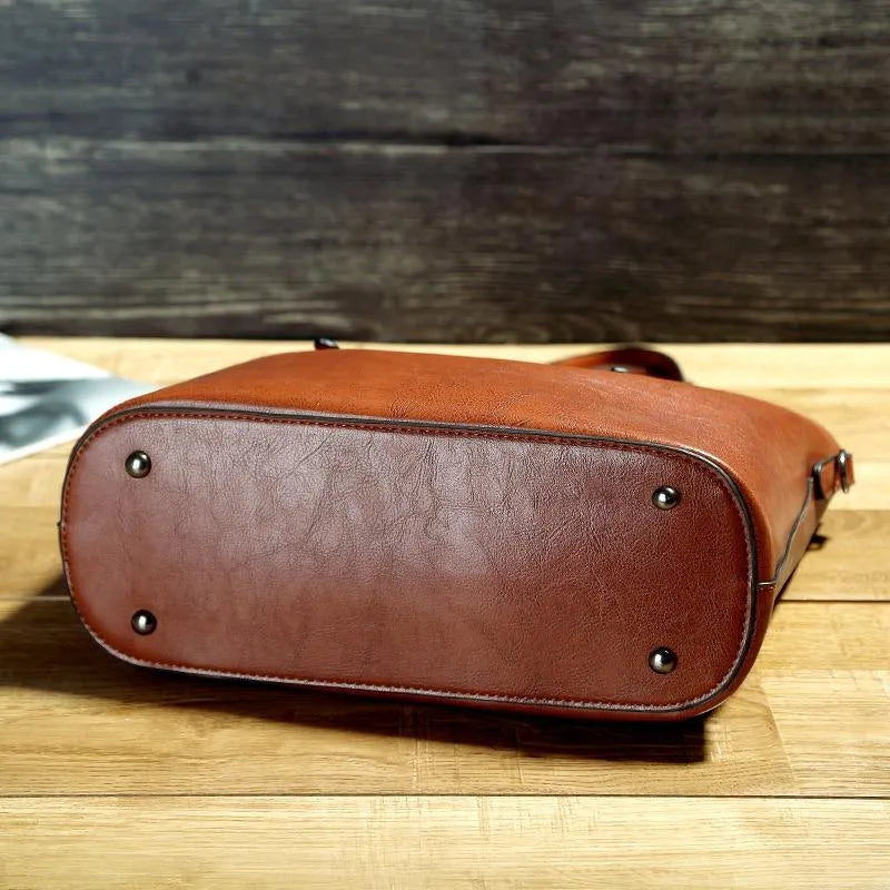 Sac à main en cuir marron sur une table en bois, avec des rivets métalliques à la base. Accessoire mode élégant et tendance pour femmes.