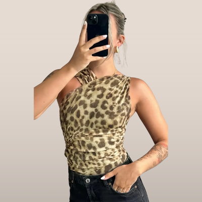 Femme portant un haut asymétrique imprimé léopard, tenant un smartphone, posant contre un fond neutre. Mode tendance, style animalier, tenue chic.