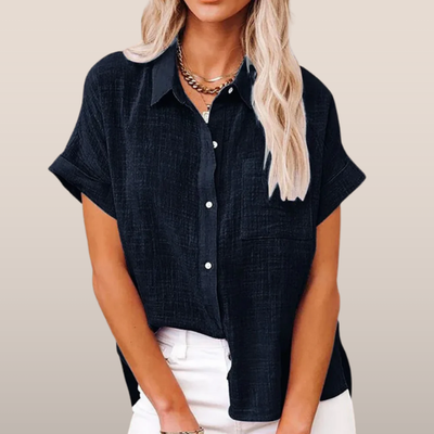 Chemisier noir à manches courtes pour femme, col classique, boutons blancs, porté avec un pantalon blanc. Mode féminine élégante et décontractée.