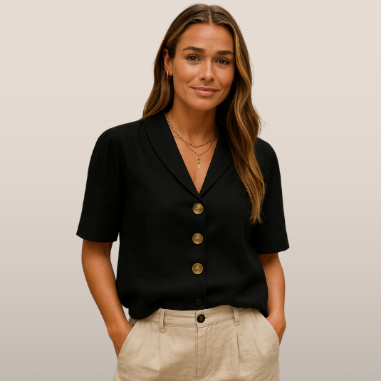 Femme portant une chemise noire à boutons dorés et un pantalon beige, posant devant un fond neutre. Mode élégante, tenue décontractée chic.