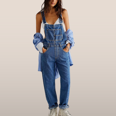 Femme en salopette en jean bleu, chemise bleue nouée à la taille, baskets blanches. Mode décontractée, tendance denim, style urbain.