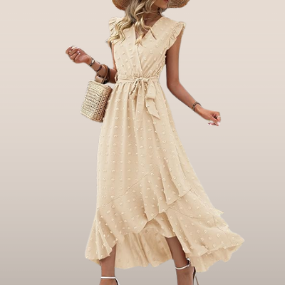 Robe longue beige à volants, ceinture nouée, motifs à pois, portée avec un chapeau de paille et un sac en osier. Mode estivale élégante et féminine.