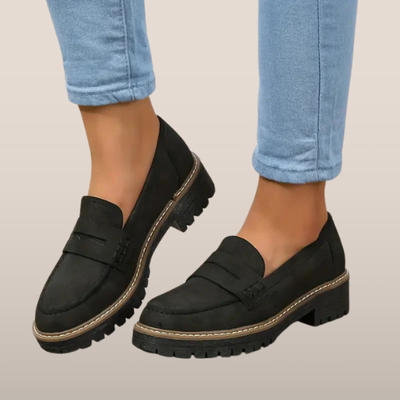 Chaussures mocassins noirs pour femmes, semelle épaisse, portées avec un jean bleu clair. Style décontracté et moderne, idéal pour l'automne.