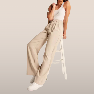 Femme en débardeur blanc et pantalon beige ample, assise sur une échelle blanche, baskets blanches. Mode décontractée, style chic et moderne.
