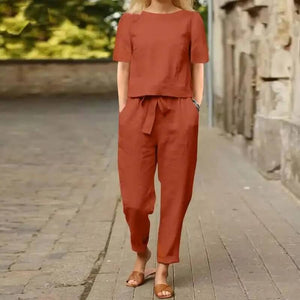 Femme en ensemble décontracté en lin rouge brique, marchant sur une rue pavée. Mode estivale, tenue confortable, style urbain chic.